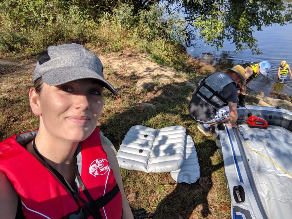 Selfie of Jacqueline with Ben and one child in the background pumping the boat while the other child plays in the water. 