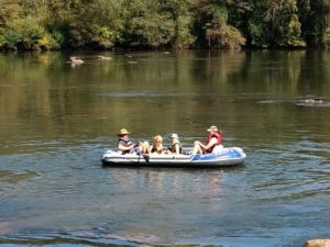 Small raft with 2 adults and two kids in it. Oars on one side being handled by dad. 